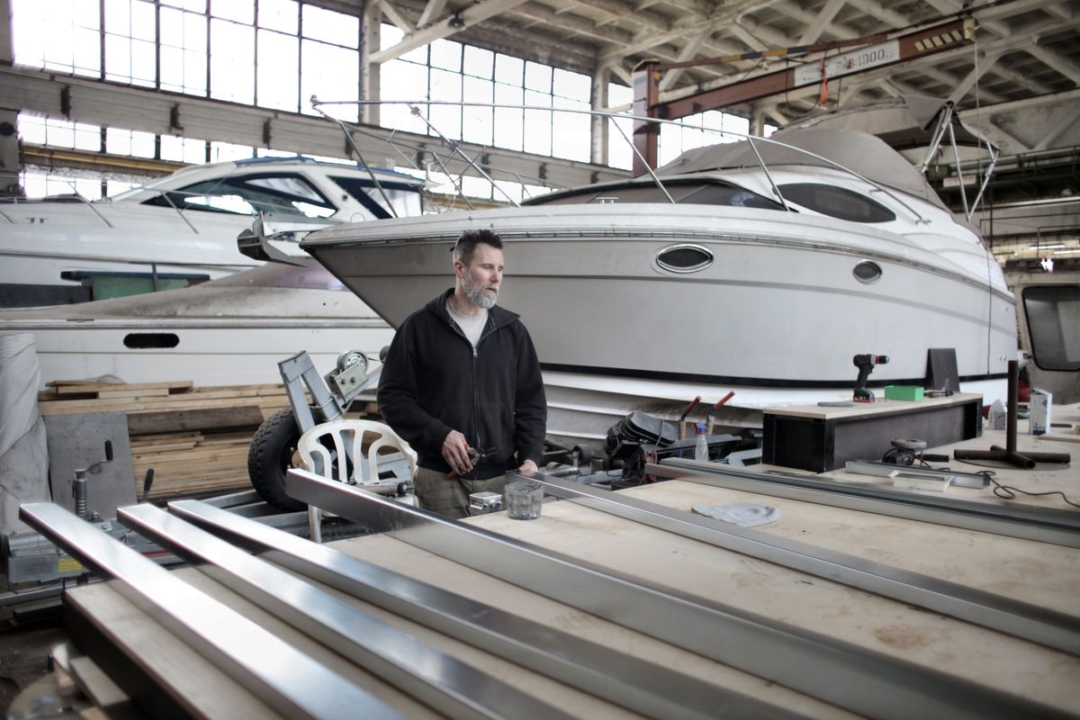 Marine mechanic in large workshop with boats on stands